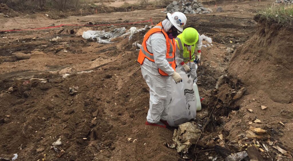 Workers in protective suits and high-visibility safety gear collecting contaminated soil and debris at an active excavation site, showcasing Halker’s environmental remediation, site restoration, and construction management expertise for complex cleanup projects.