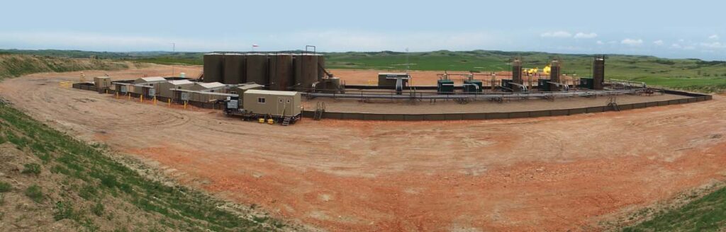 Large oil and gas production facility with storage tanks, process equipment, and a centralized operations trailer set against open field terrain, showcasing Halker’s strategic field development expertise in planning, designing, and optimizing multi-well production sites for efficient and scalable operations.