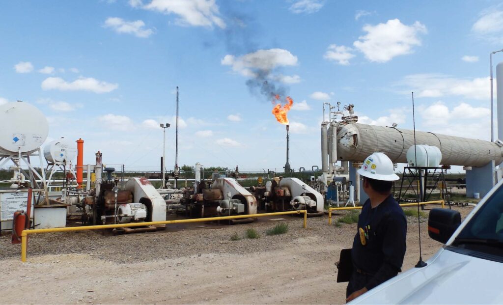 Field engineer observing an active flare stack alongside compressors and process equipment at a midstream facility, highlighting Halker’s expertise in flare system retrofits, combustion safety improvements, and emissions-compliant facility upgrades.