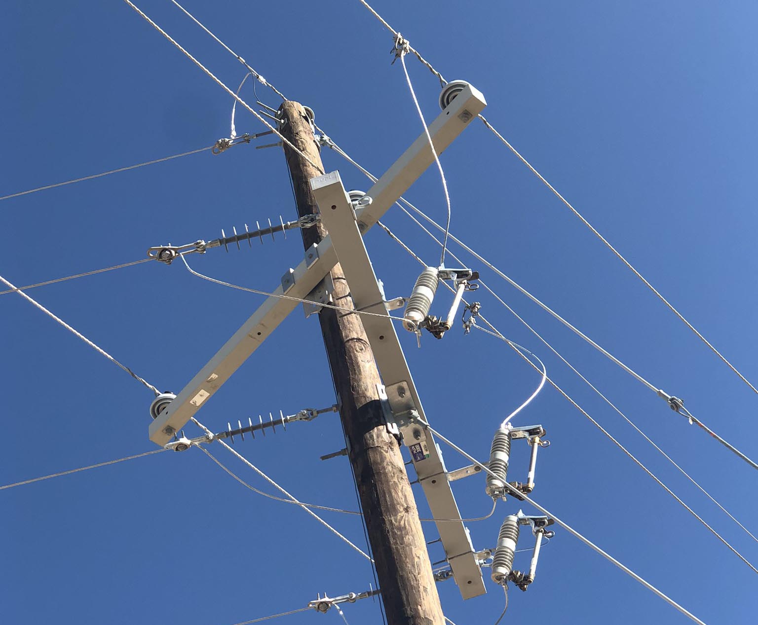 Overhead power distribution pole equipped with sectionalizing fuses, insulators, and energized conductors against a clear blue sky, showcasing Halker’s expertise in electrical engineering, grid reliability improvements, and utility distribution system design.