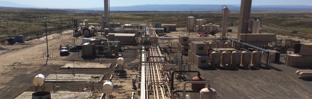 Midstream facility with interconnected process piping, tanks, and equipment set against a wide-open landscape, highlighting Halker’s expertise in facilities conversion, system upgrades, and engineering solutions tailored to evolving operational needs.