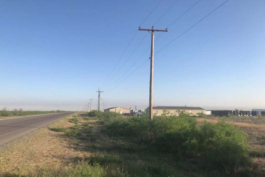Rural power distribution line with wooden utility poles running alongside a roadway and open field, demonstrating Halker’s field inspection and evaluation expertise for electrical infrastructure reliability, safety, and system performance.