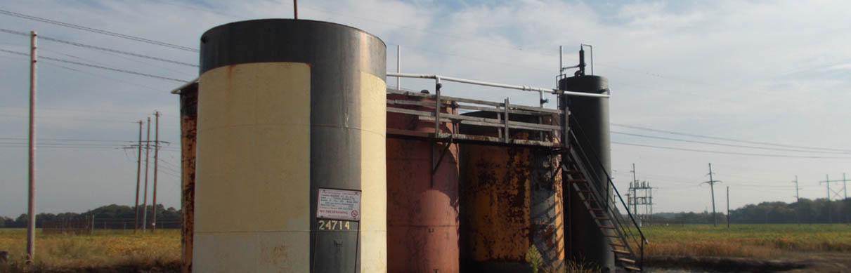 Aging above-ground storage tanks with visible corrosion, access platforms, and identification signage, illustrating Halker’s regulatory and environmental site review expertise in assessing legacy oil and gas infrastructure for compliance, safety risks, and remediation needs.