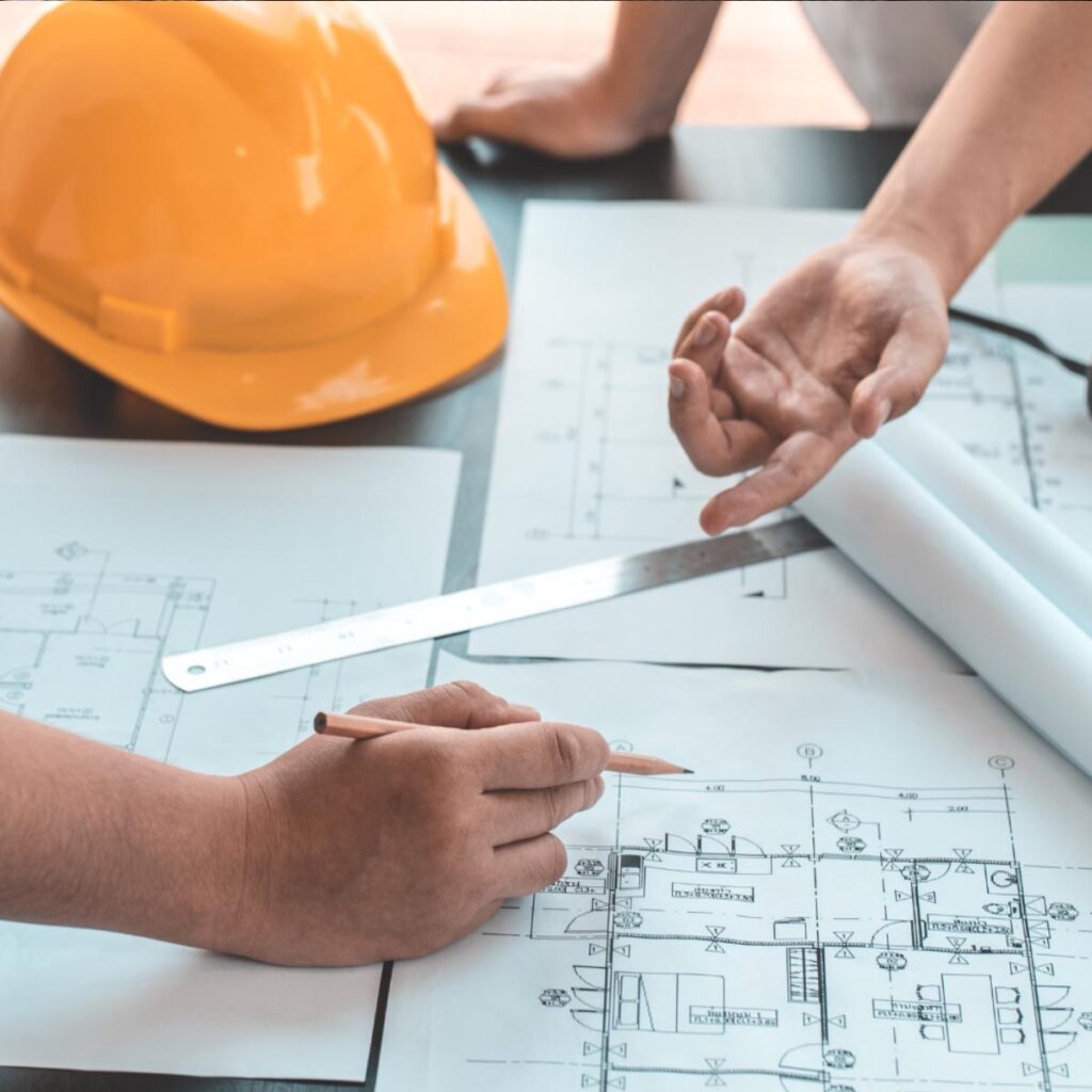 Engineers reviewing technical drawings and construction blueprints alongside a hard hat and drafting tools, highlighting Halker’s precision-driven project planning, engineering design, and multidisciplinary coordination.
