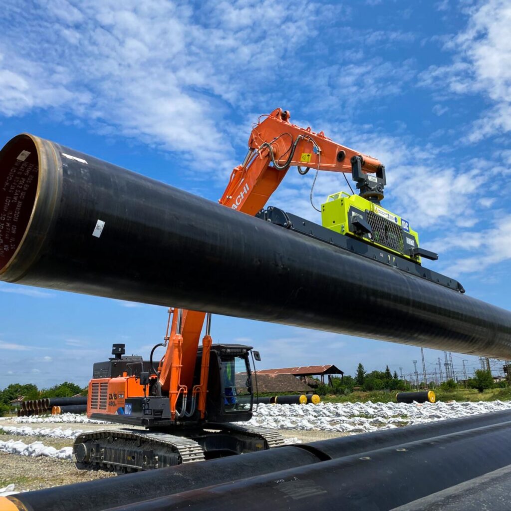 Excavator lifting and positioning a large-diameter steel pipeline segment at an active construction site, showcasing Halker’s expertise in pipeline engineering, field installation support, and procurement support.