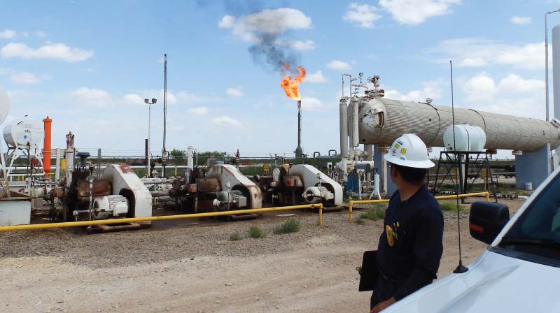 Field engineer observing active flare stack and production equipment at an upstream oil and gas facility, illustrating Halker’s expertise in site assessments, facility operations support, and safety-focused engineering in hydrocarbon processing environments.