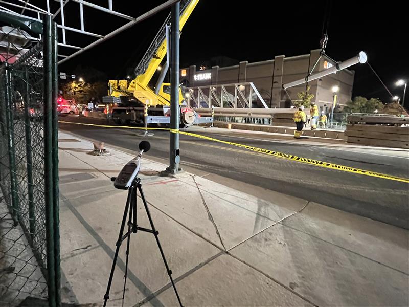 Tripod-mounted sound level meter recording nighttime construction activity with cranes and utility crews, showcasing Halker’s noise monitoring services for environmental compliance and community impact mitigation on infrastructure projects.
