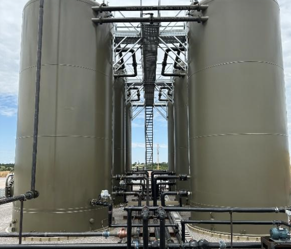 Large vertical production tanks with interconnected piping and access platforms at an oil and gas facility, illustrating Halker’s field expertise in EPA OOOOb compliance walkdowns, emissions verification, and regulatory readiness for Anadarko Basin operations.