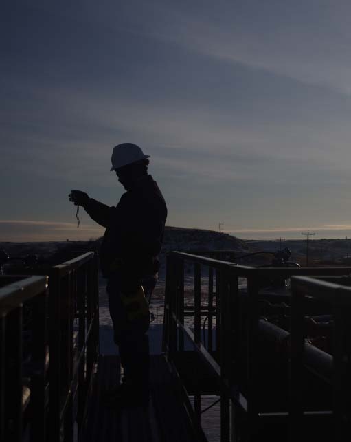 Silhouette of a field engineer wearing a hard hat and safety gear while inspecting equipment on an oil and gas facility walkway at sunrise, representing Halker's commitment to safe operations, field support, and high-quality engineering services.